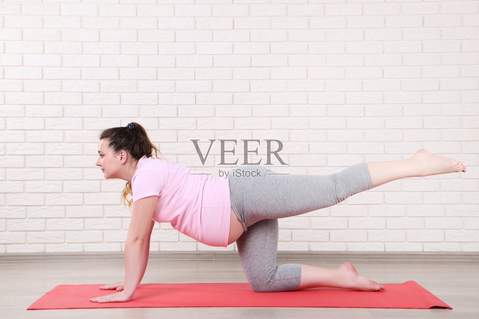 年轻孕妇在砖墙背景下做运动照片摄影图片