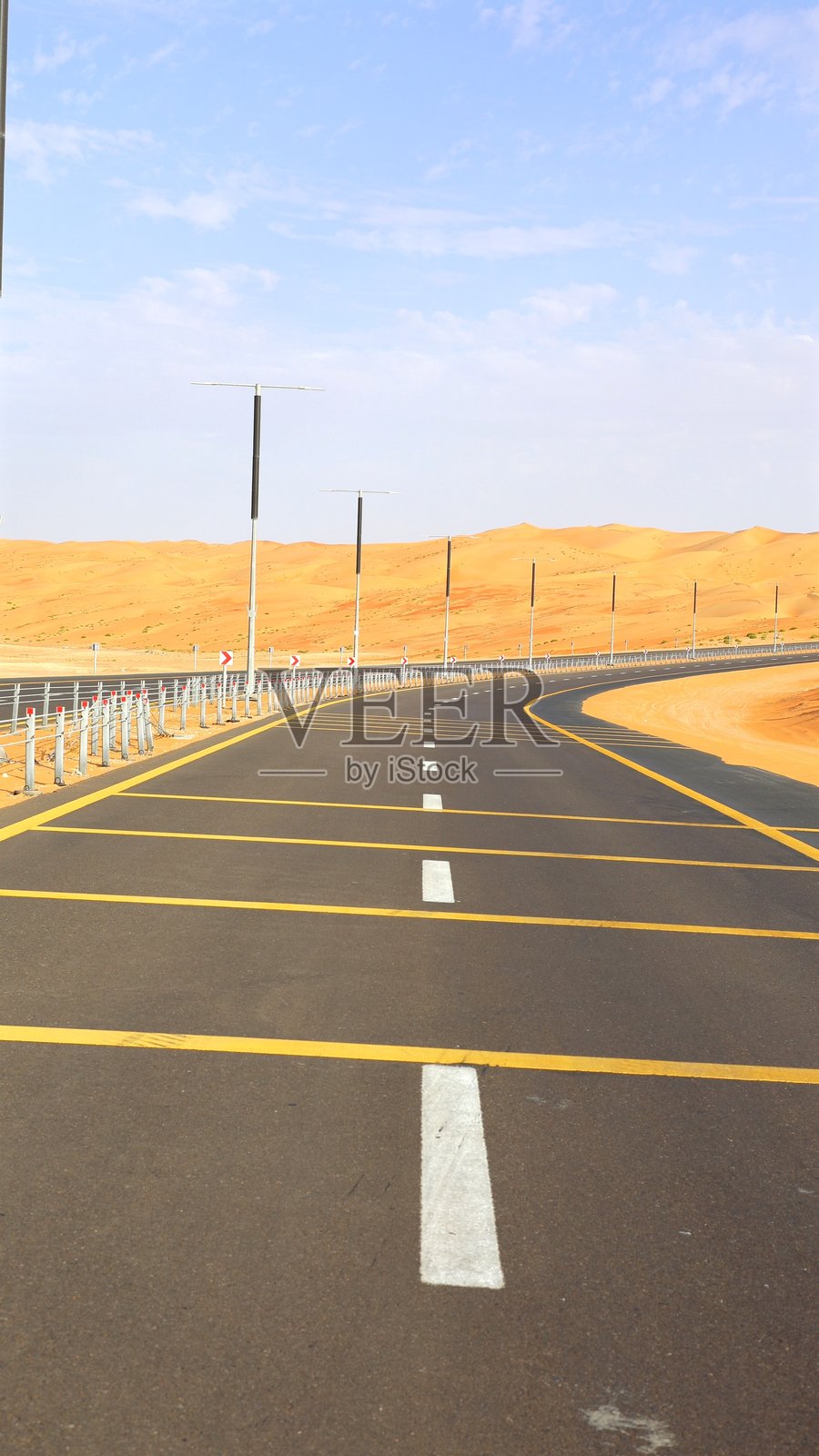 沙漠公路在柔和的蓝天下缓缓弯曲，清晰的白色和黄色标记增强了对比，公路象征着通往宁静目的地的旅程，带来宁静的旅行灵感概念。照片摄影图片