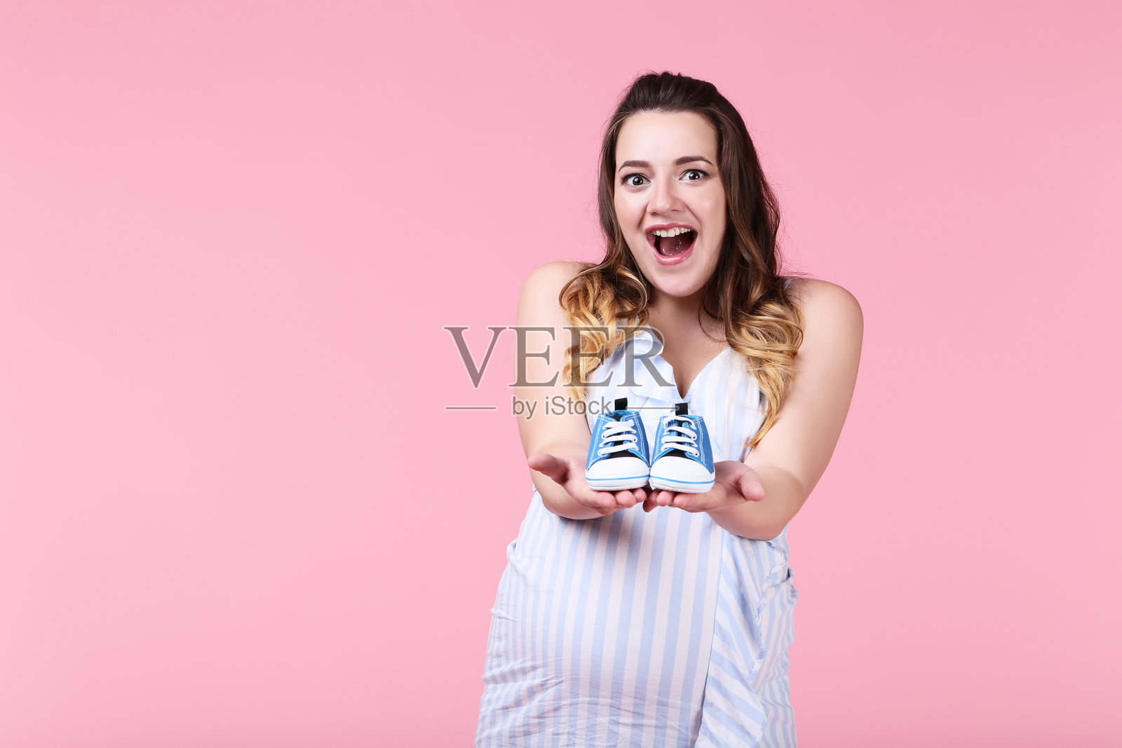 美丽的孕妇与粉色背景上的婴儿鞋照片摄影图片