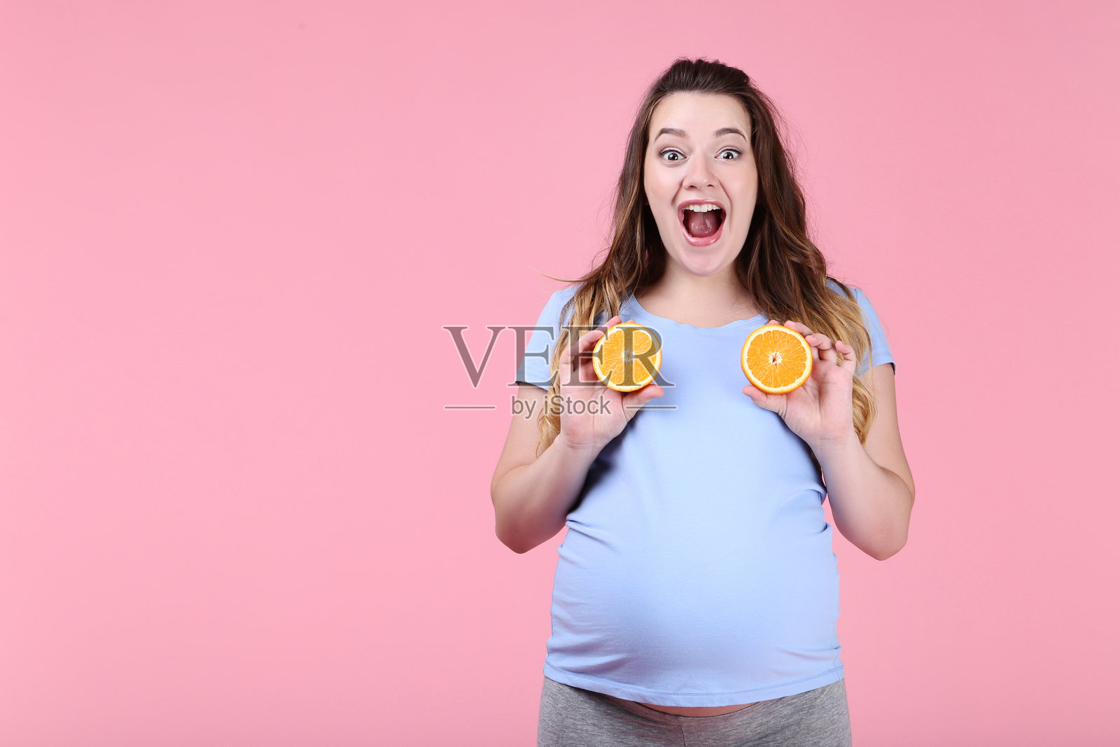 美丽的孕妇与橙色水果在粉色背景上照片摄影图片