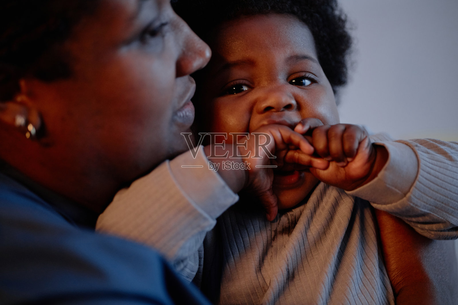 室内黑肤小女孩咬手指坐在母亲的手上照片摄影图片