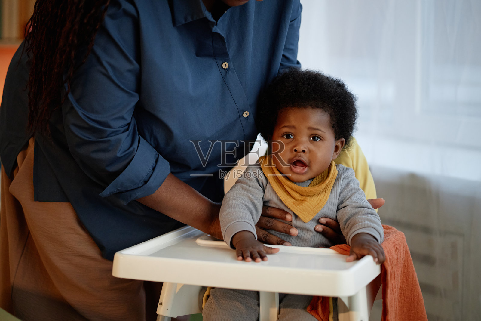 黑人母亲将女婴放入高脚椅，为女儿准备用餐时间在厨房里照片摄影图片