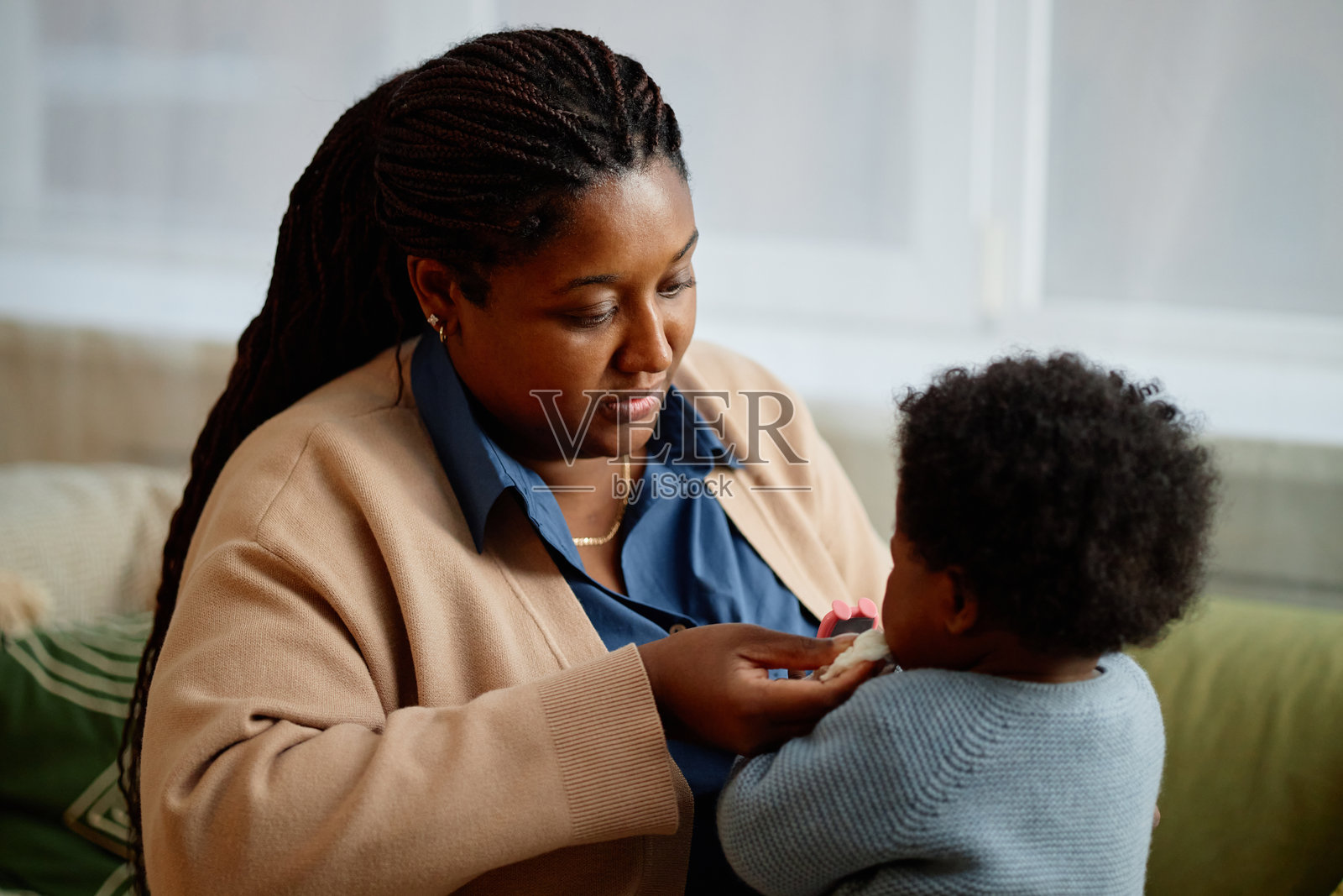 黑人母亲在家沙发上给女婴喂牙胶玩具照片摄影图片