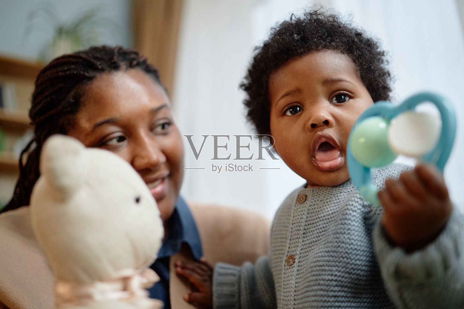 母亲在家里和黑肤色的小女孩玩耍，小女孩手里拿着咬咬乐。照片摄影图片