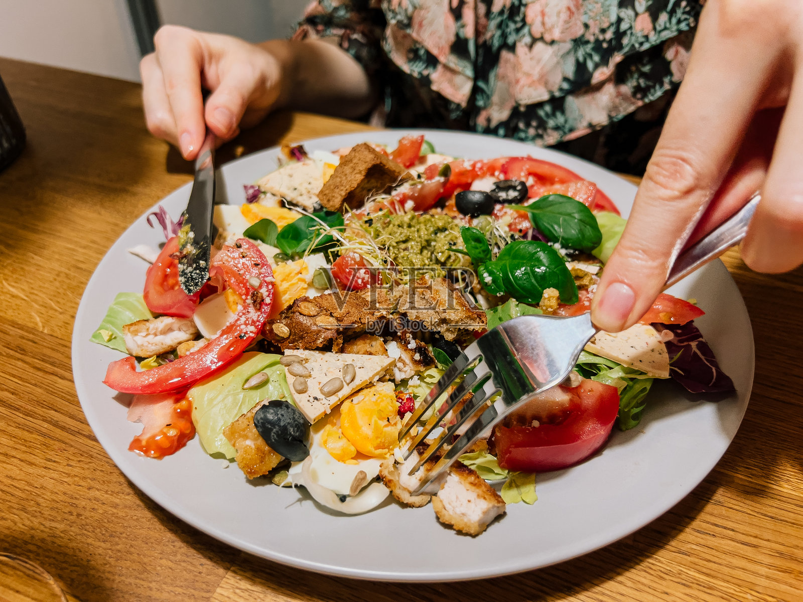 女人在家中用刀叉吃自制沙拉，享受着番茄和绿叶的美味，盘子里盛满新鲜的口味和天然的食材。咬一口色彩缤纷的食物，里面有鸡蛋和香蒜酱，营造出温馨的家庭氛围。照片摄影图片