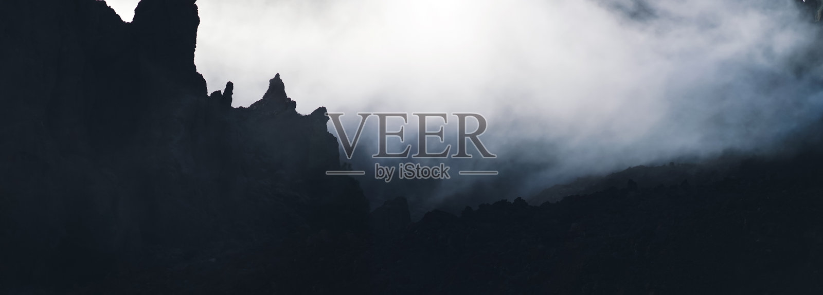 神秘的风景，雾中有黑色轮廓的岩石山脉。照片摄影图片