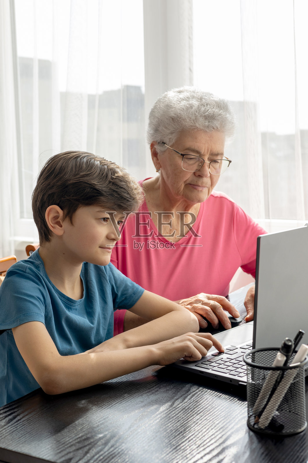 年轻男孩教他的祖母电脑技能——跨代数字素养。老年人的教育。数字素养。老年人使用笔记本电脑。代际互动。照片摄影图片