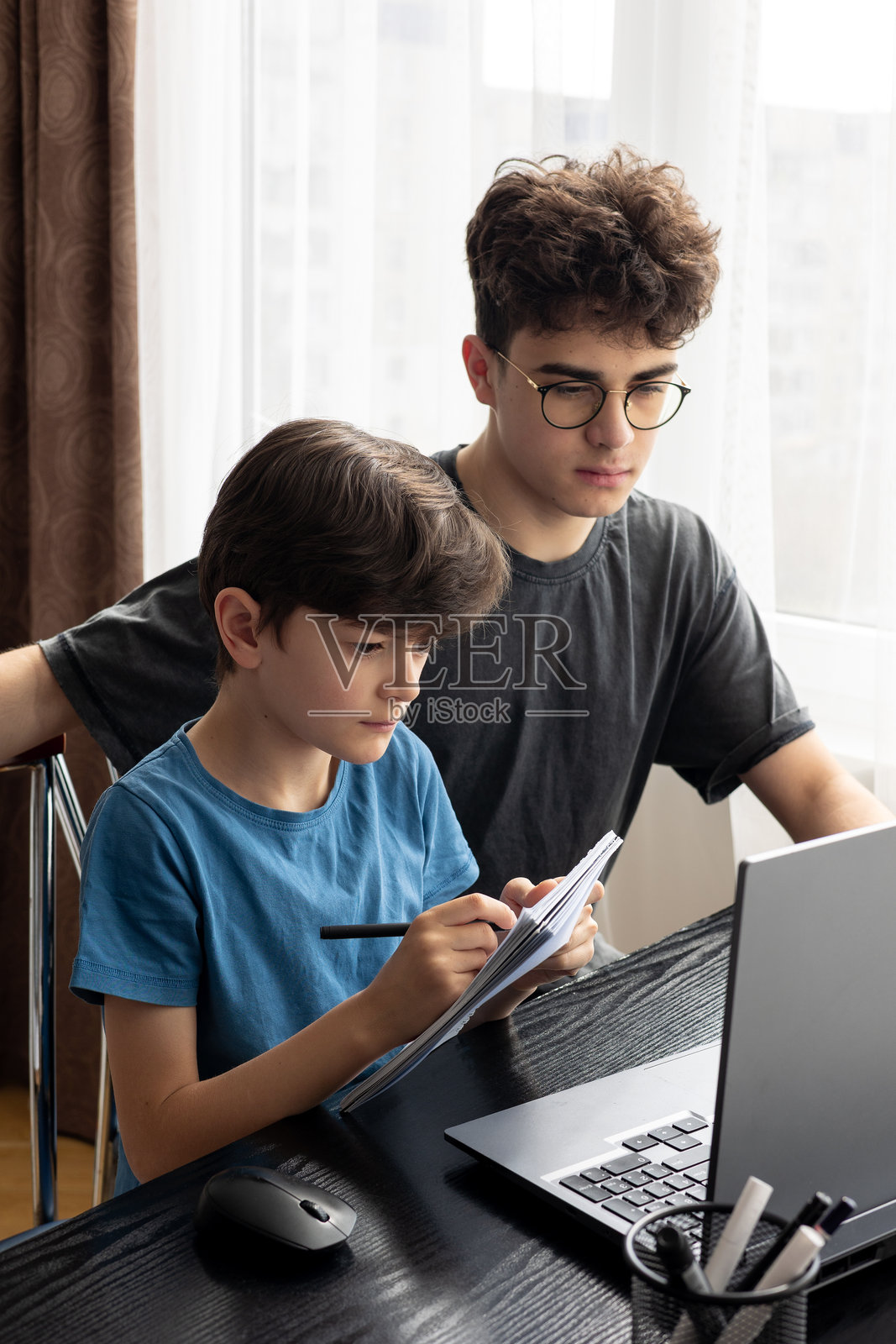 两个兄弟专注于笔记本电脑屏幕，沉浸在思考和学习中。在线学习。远程教育。代际互动。现代儿童与电子设备。学习时的专注。照片摄影图片