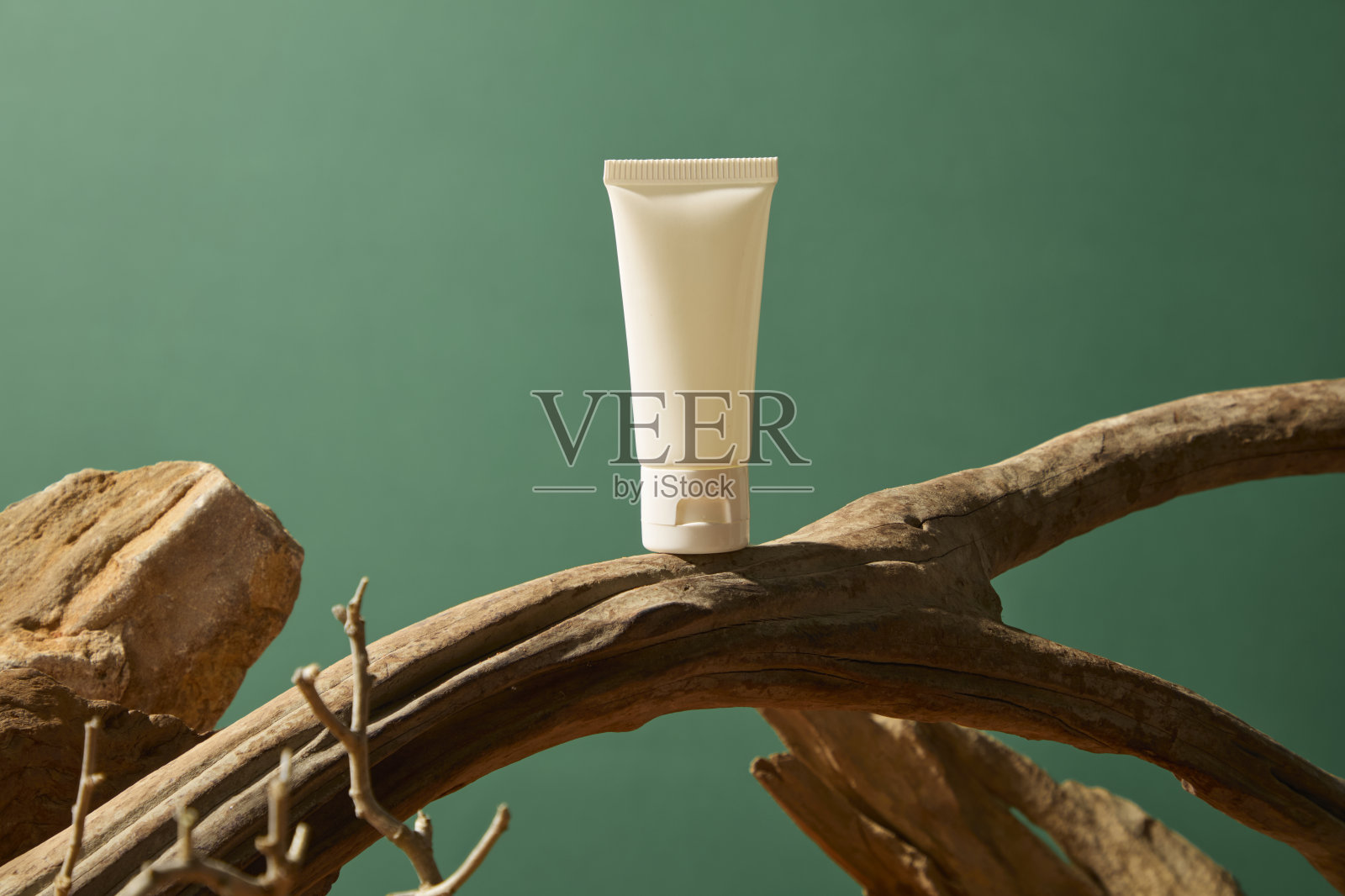 粗糙的树枝上有沿着树干延伸的空心线条，弯曲成一个圆圈。化妆品管放置在弯曲的树干上，周围是干旱的树林。色彩鲜艳的岩石形成了一座山。照片摄影图片