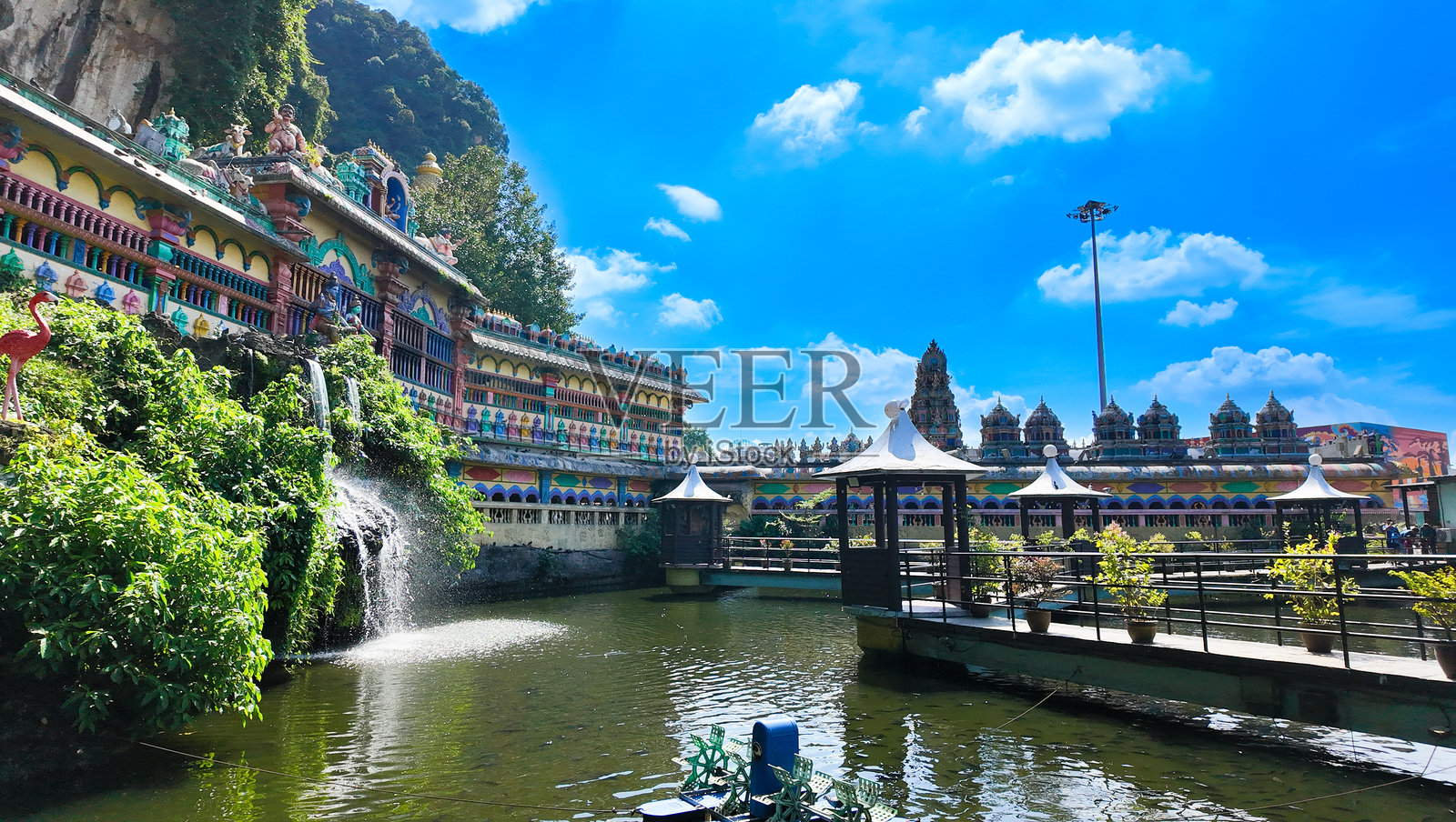 马来西亚巴图洞别墅附近的池塘，四周环绕着郁郁葱葱的绿树，有瀑布、桥梁和凉亭，靠近一座印度教寺庙。照片摄影图片