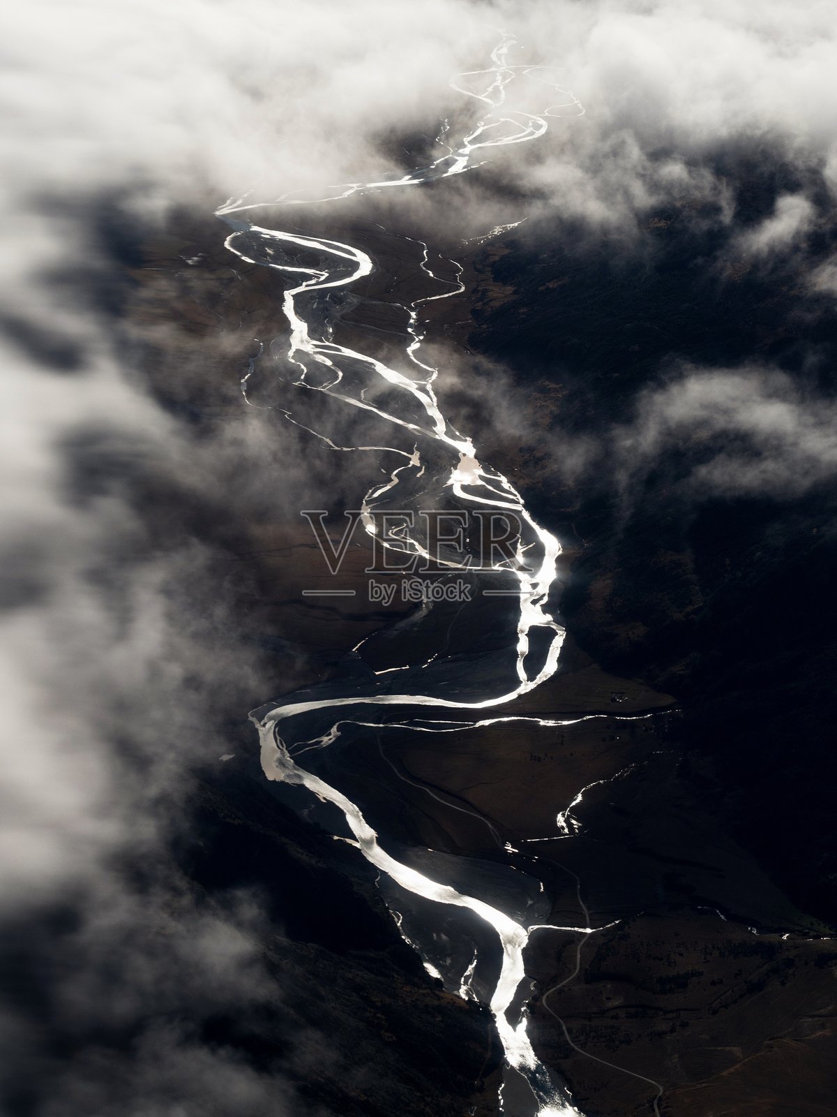 从空中俯瞰，河流蜿蜒穿过南阿尔卑斯山谷，云层之下，位于新西兰南岛的奥塔哥南部。照片摄影图片