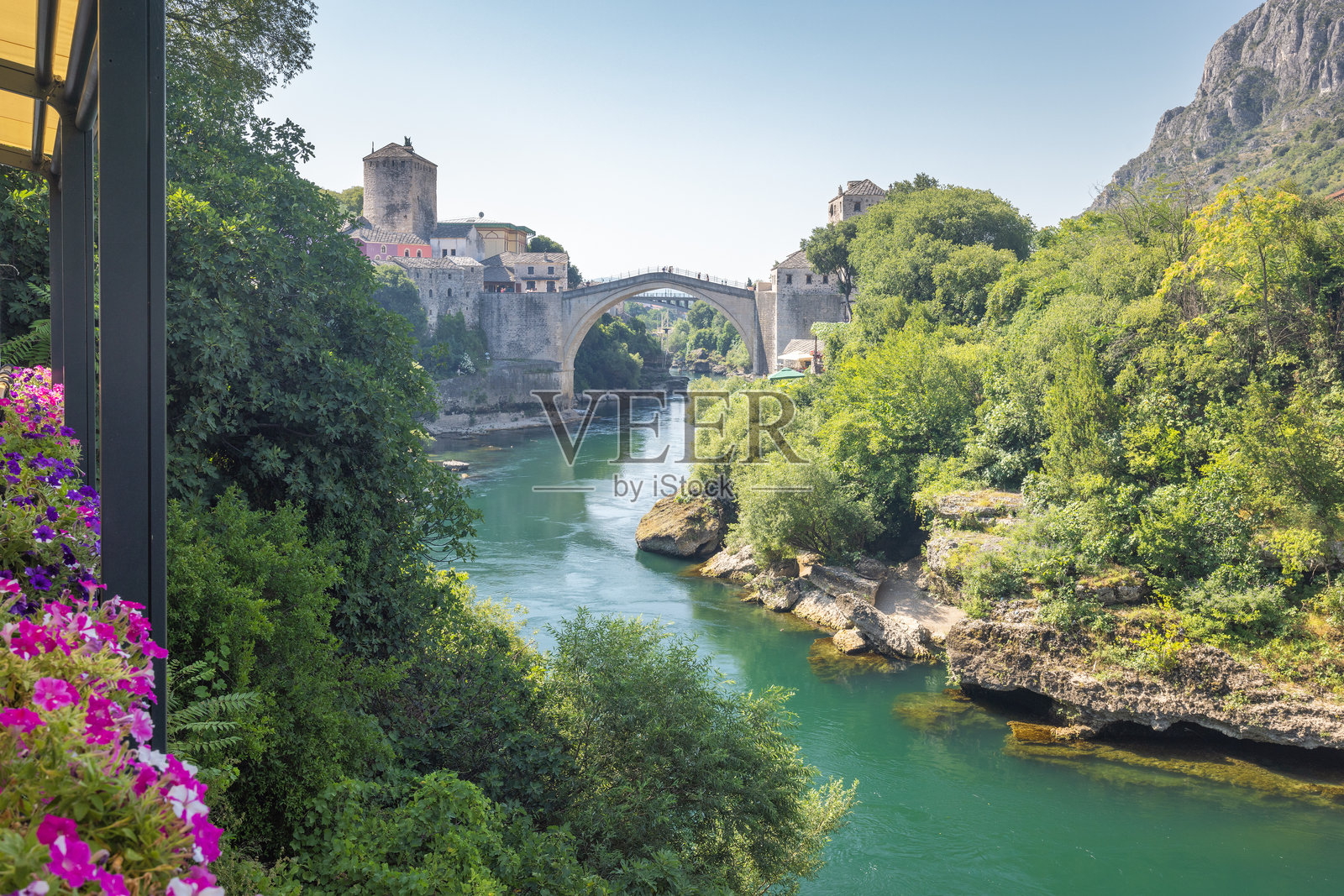 波斯尼亚和黑塞哥维那莫斯塔尔镇的斯塔里桥，横跨内雷特瓦河。古老的桥梁拱形跨越河流，两侧是历史建筑和郁郁葱葱的绿树，阳光明媚。照片摄影图片