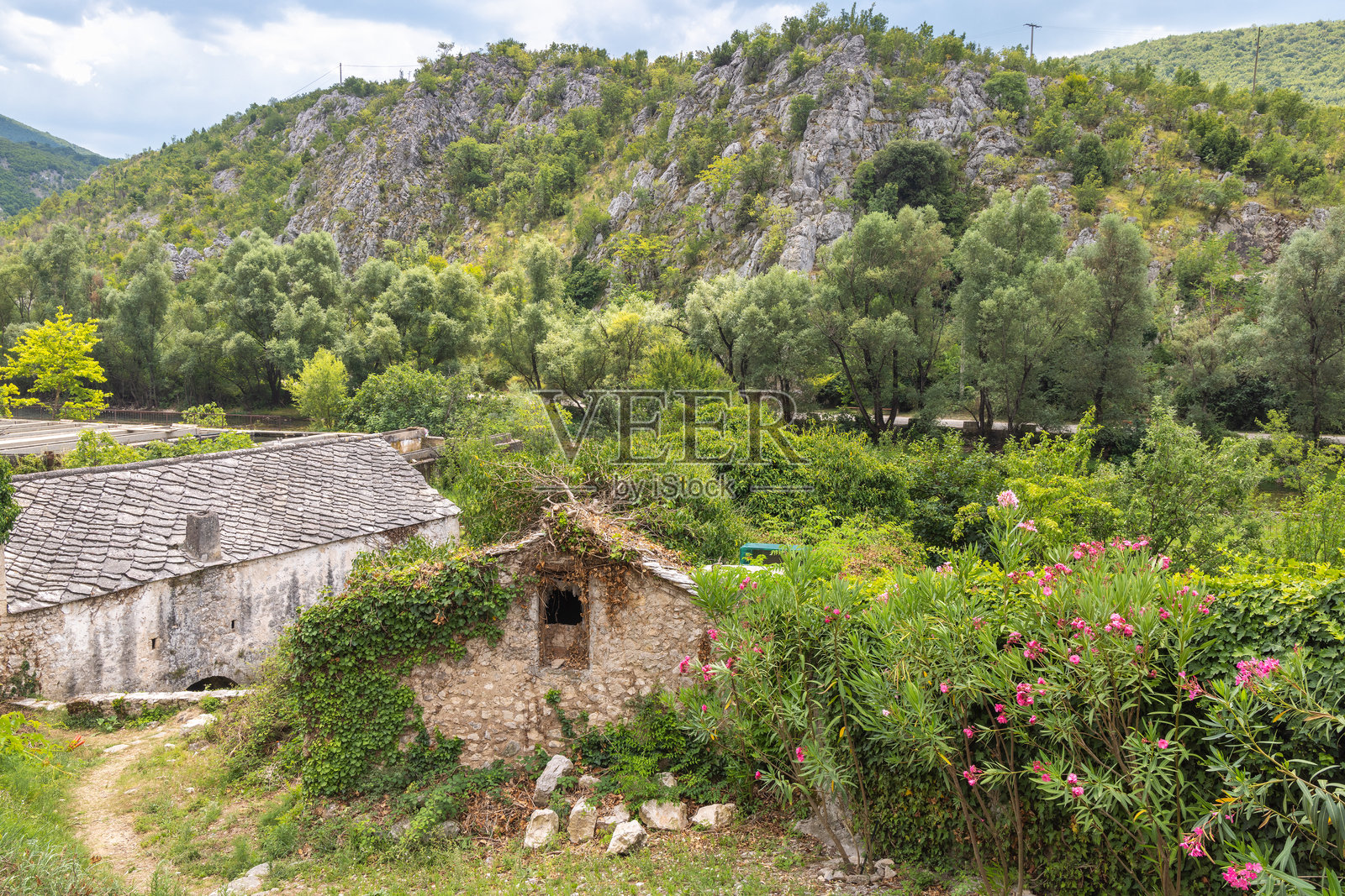 波斯尼亚和黑塞哥维那布拉加伊村的古老石屋。被郁郁葱葱的绿树环绕的石建筑依偎在岩石山丘下，唤起一种隐秘的宁静和被遗忘的魅力。照片摄影图片