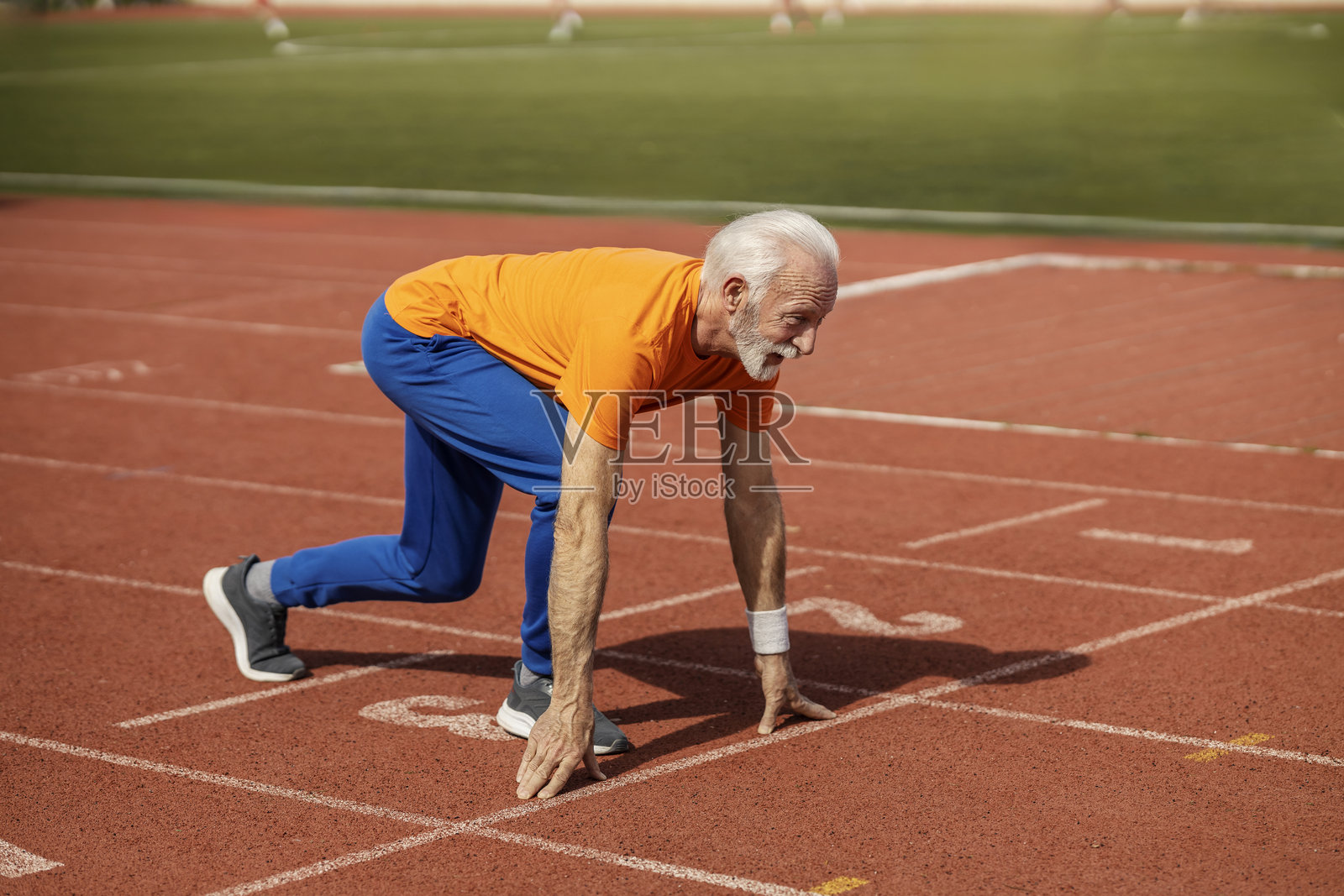 老运动员在体育场的起跑位置准备奔跑。照片摄影图片