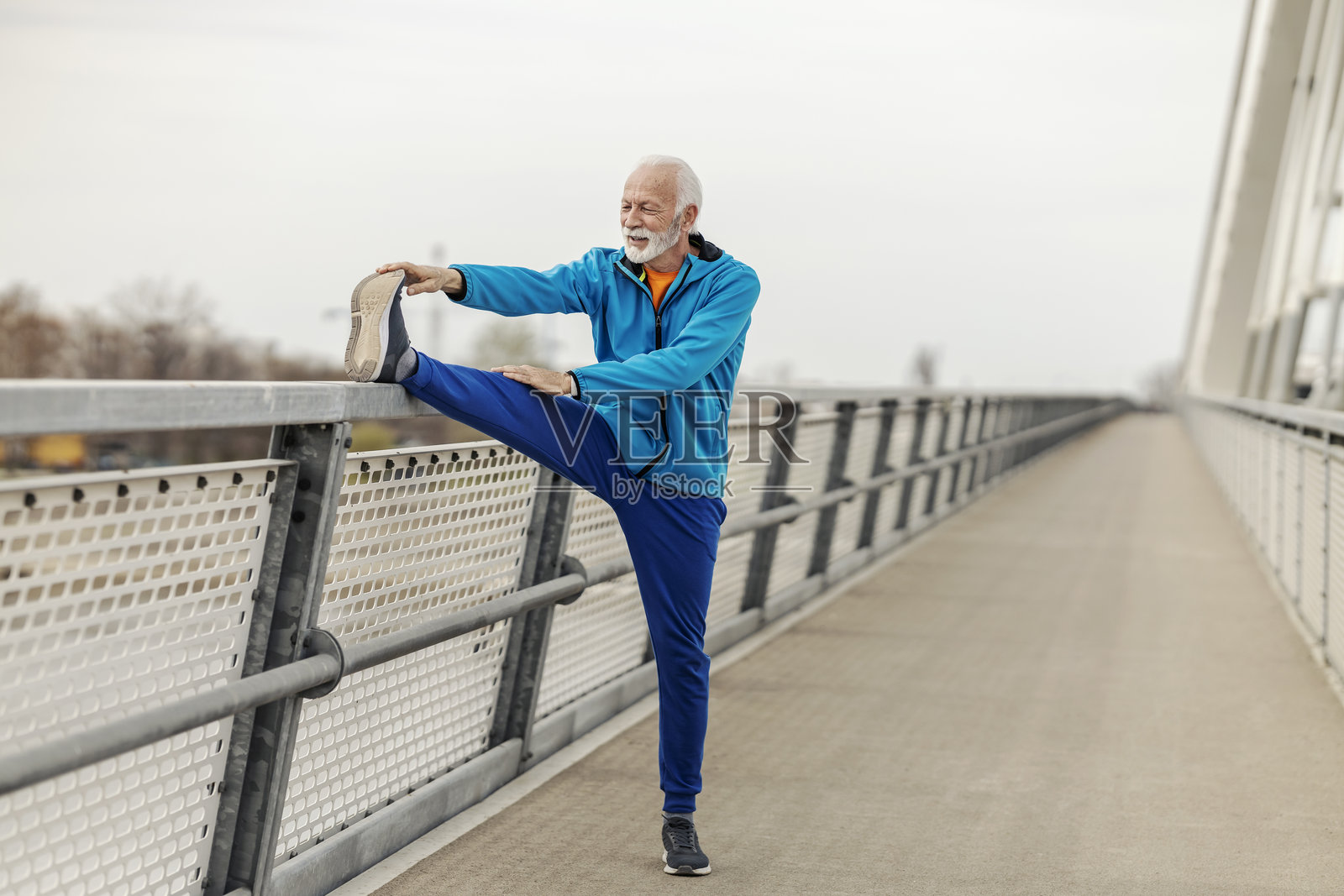 身材健壮的老年运动员在桥上拉伸腿部。照片摄影图片