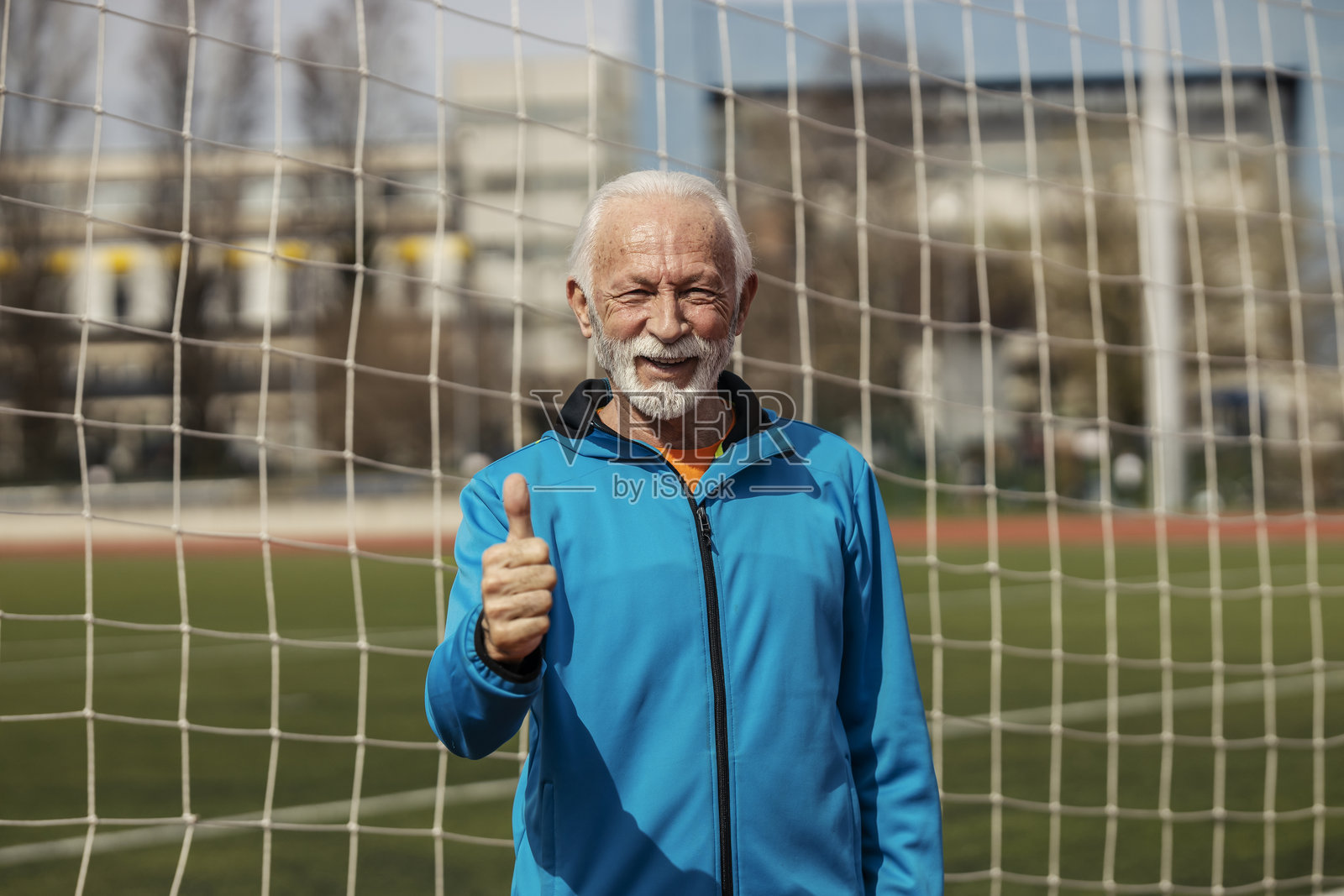 身穿运动服的资深运动员站在体育场上，竖起大拇指，倡导积极健康的生活方式。照片摄影图片