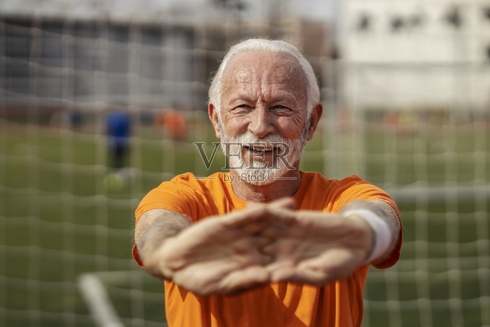 健康、健美、快乐的老年运动员在体育场伸展双臂并对着镜头微笑的肖像。照片摄影图片