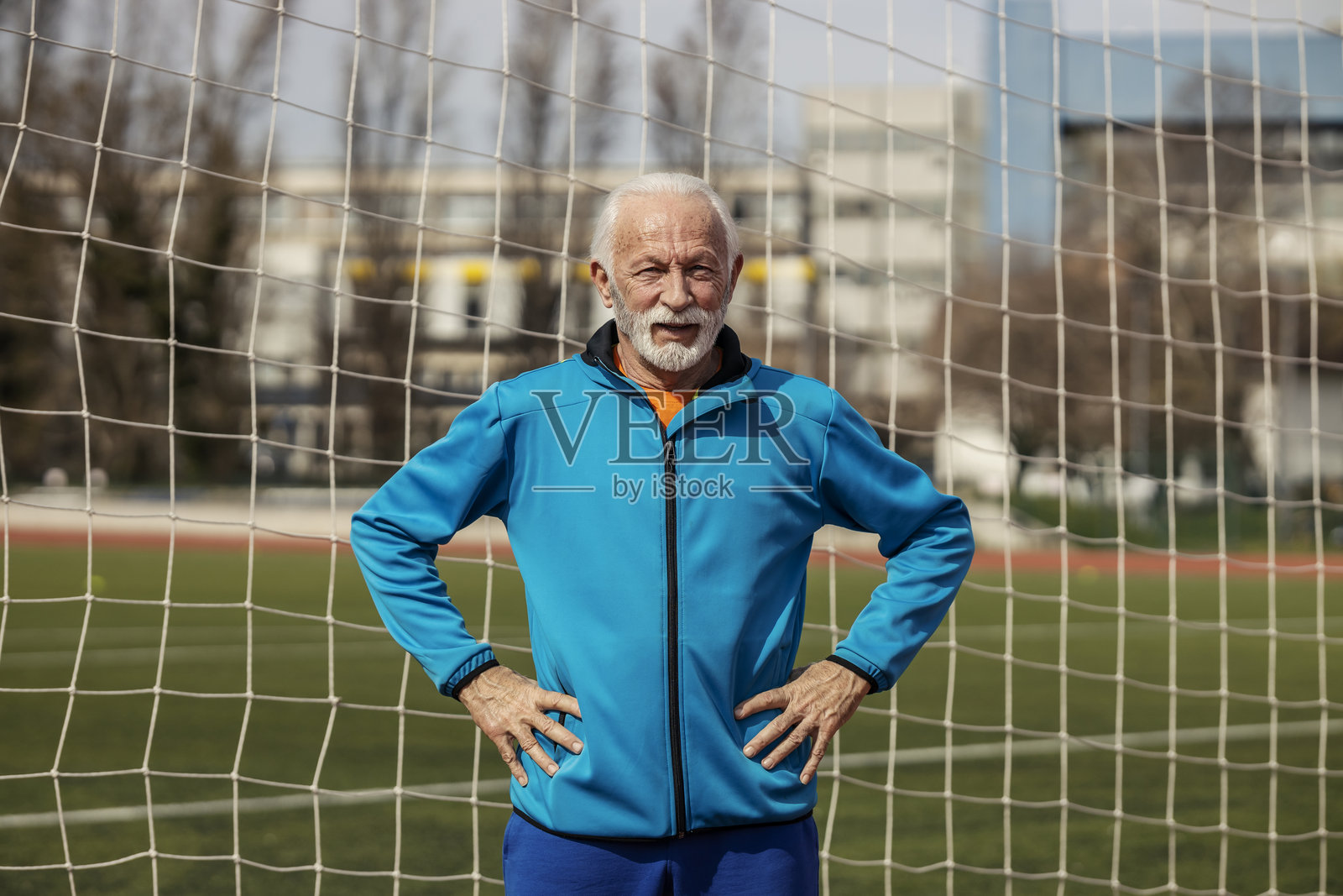 疲惫的老年运动员站在体育场上，双手叉腰，注视着镜头。照片摄影图片