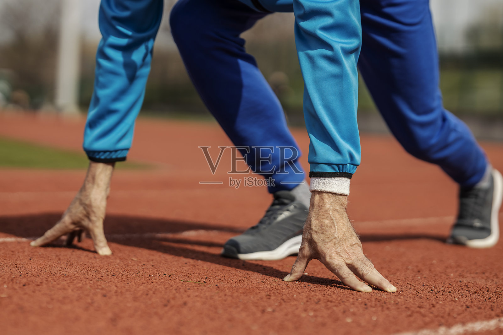 裁剪后的老年运动员在体育场起跑线准备跑步的照片。照片摄影图片