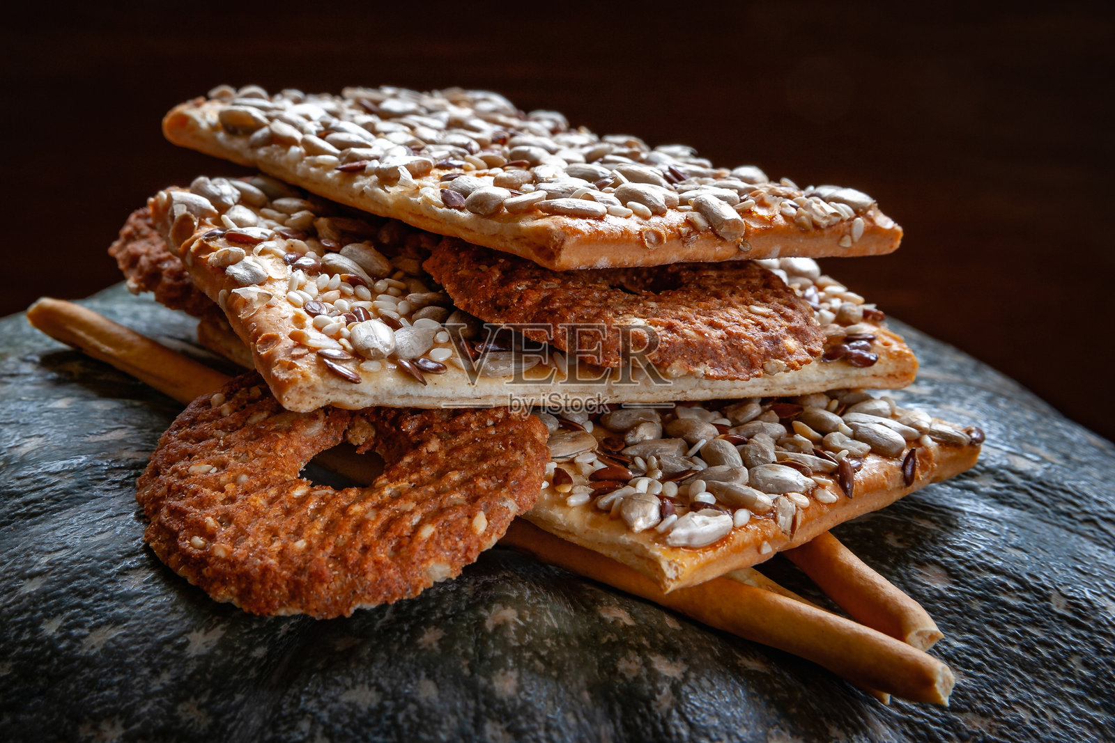 酥脆的饼干饼干，上面撒有亚麻籽、向日葵种子和芝麻，背景是深色的南瓜。日光，选择性对焦。照片摄影图片