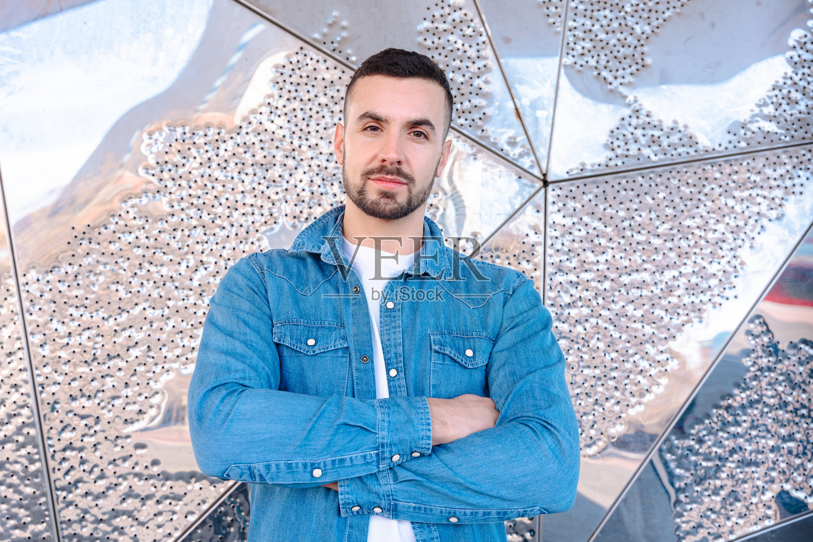 自信的白人男性双臂交叉，站在抽象金属背景前照片摄影图片