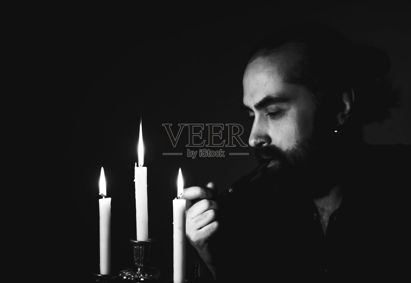 在黑暗的房间里，男人在烛光下点燃烟斗照片摄影图片