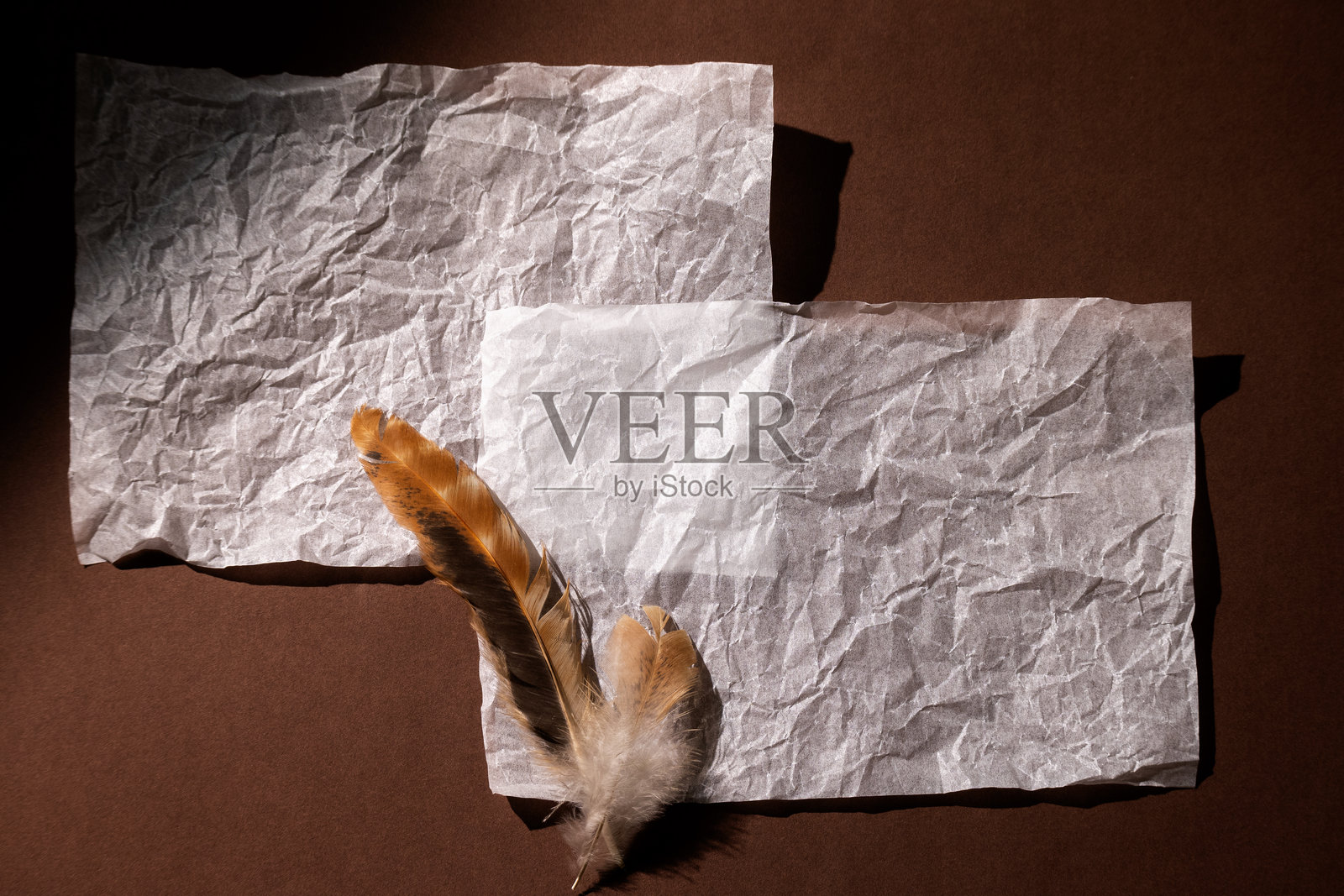 温暖的棕色背景上放着一张空白纸和一根羽毛。俯视图，简约舒适的复古风格，温暖的色调，留有文字空间。照片摄影图片