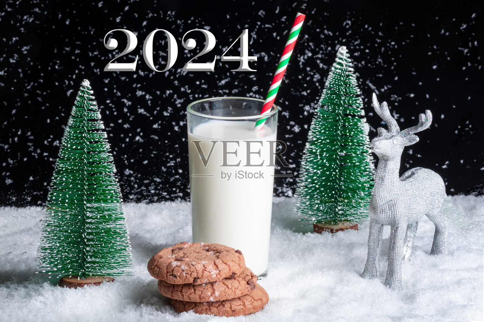 一杯牛奶配吸管和饼干，背景是雪景和玩具圣诞树。2024年新年照片摄影图片