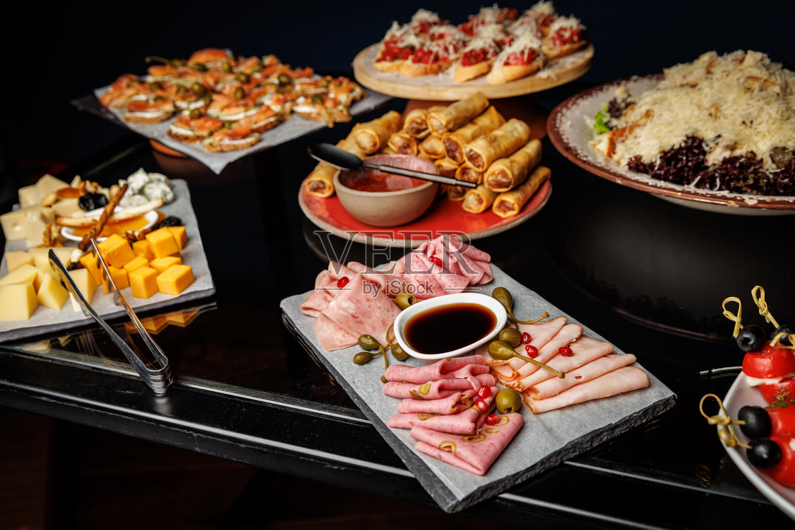桌子上摆放着各种开胃菜和小吃，包括冷切肉、奶酪块和春卷。照片摄影图片