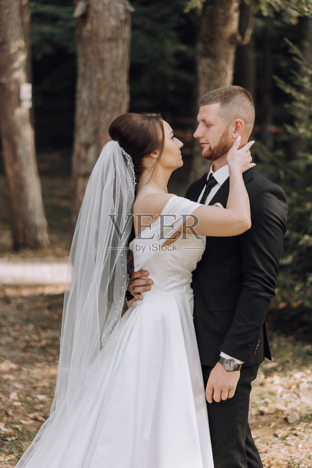 一对新郎新娘站在森林中，新娘穿着白色婚纱。照片摄影图片