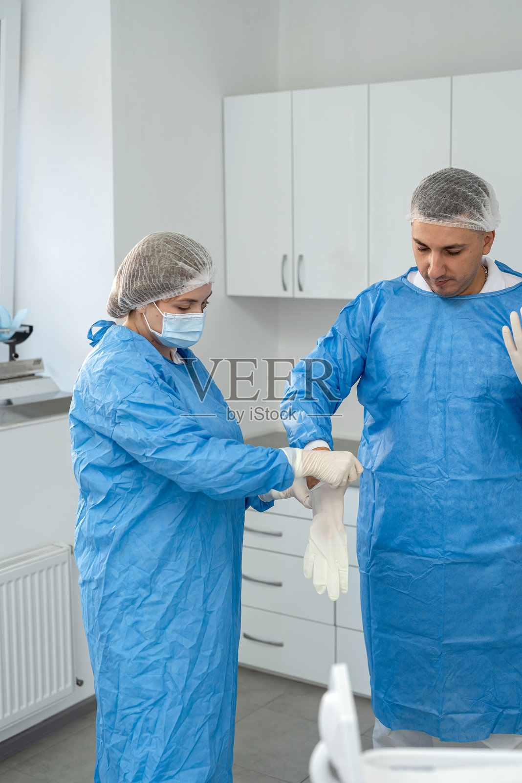 男外科医生与他的女性助手正在准备手术，穿上无菌衣。医疗概念照片摄影图片