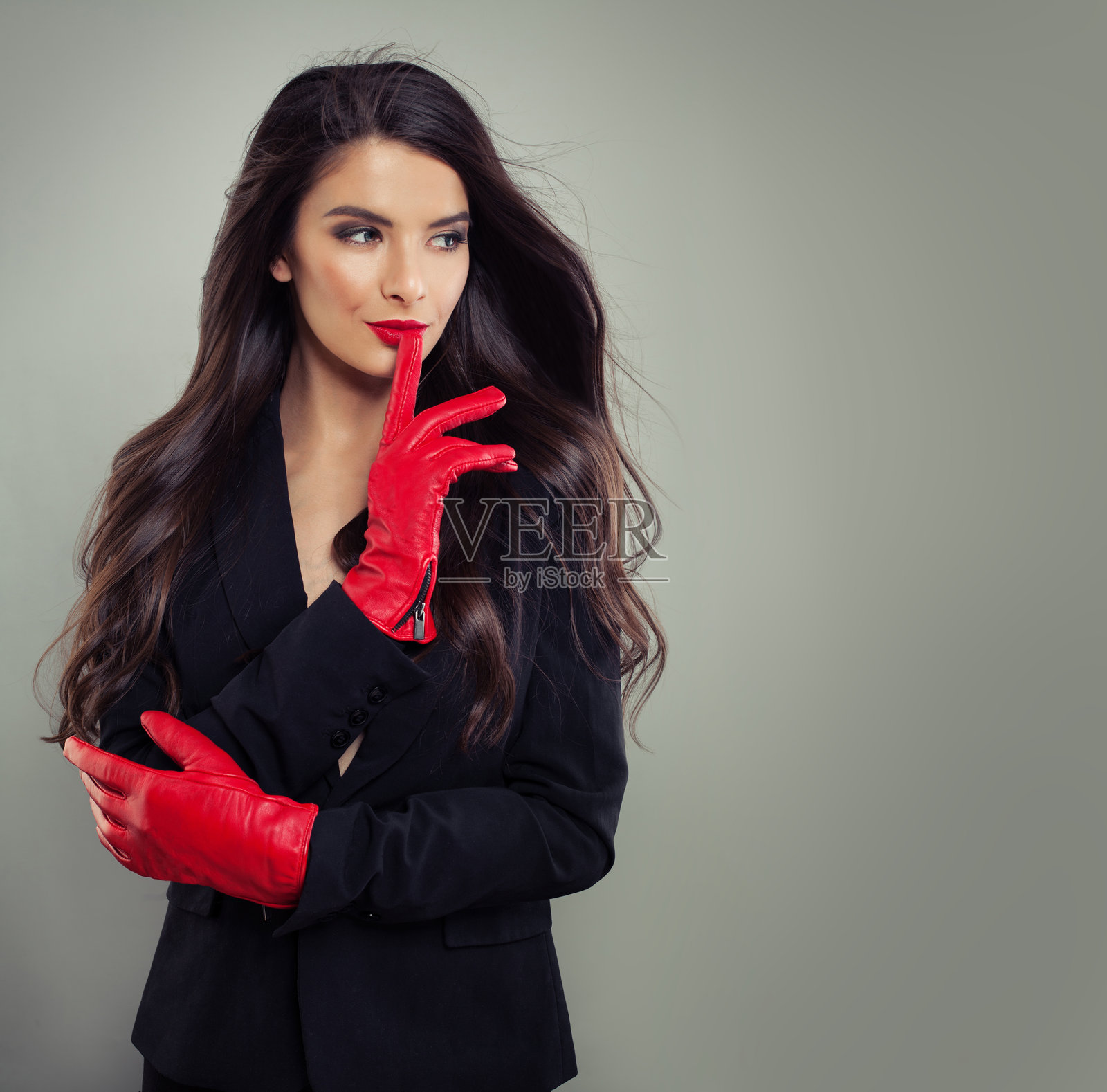 穿着黑色西装、戴着红色皮手套的时尚快乐女性，化着妆，黑发，室内摆姿势。照片摄影图片