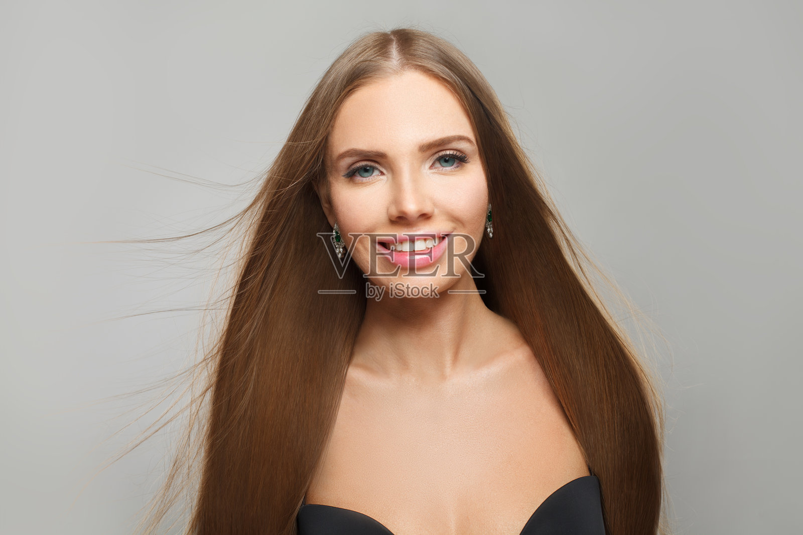 迷人的年轻女性模特，拥有现代妆容和长直顺滑的发型，站在白色摄影棚背景前。照片摄影图片