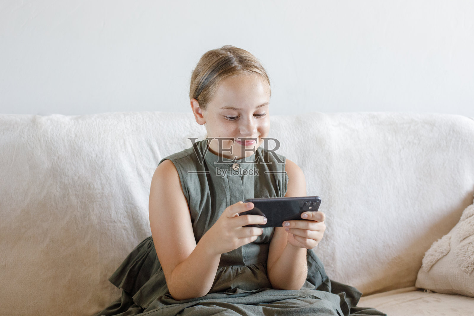 可爱的小女孩在家中使用智能手机观看卡通或玩手机游戏，室内肖像照片摄影图片