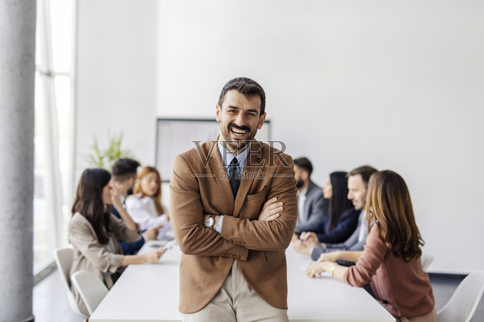 成功年轻商人在会议室中双臂交叉，站立于会议期间。照片摄影图片