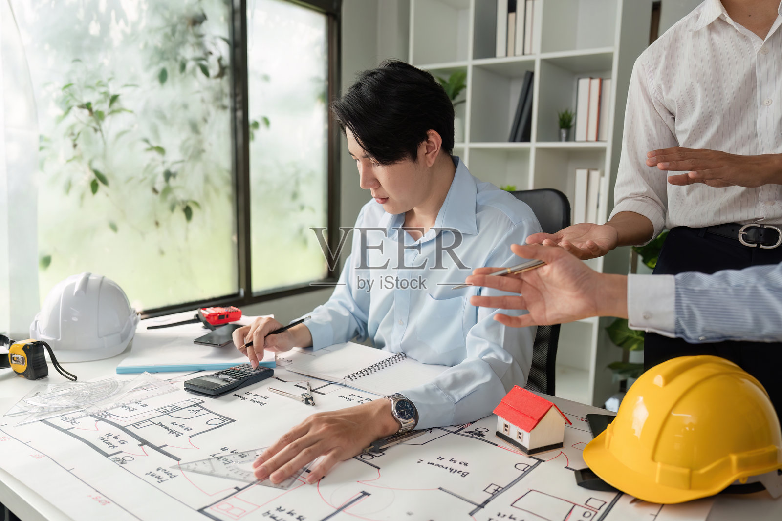 设计开发与协作。一位建筑师在现代办公室中分析项目设计，与团队成员讨论。照片摄影图片