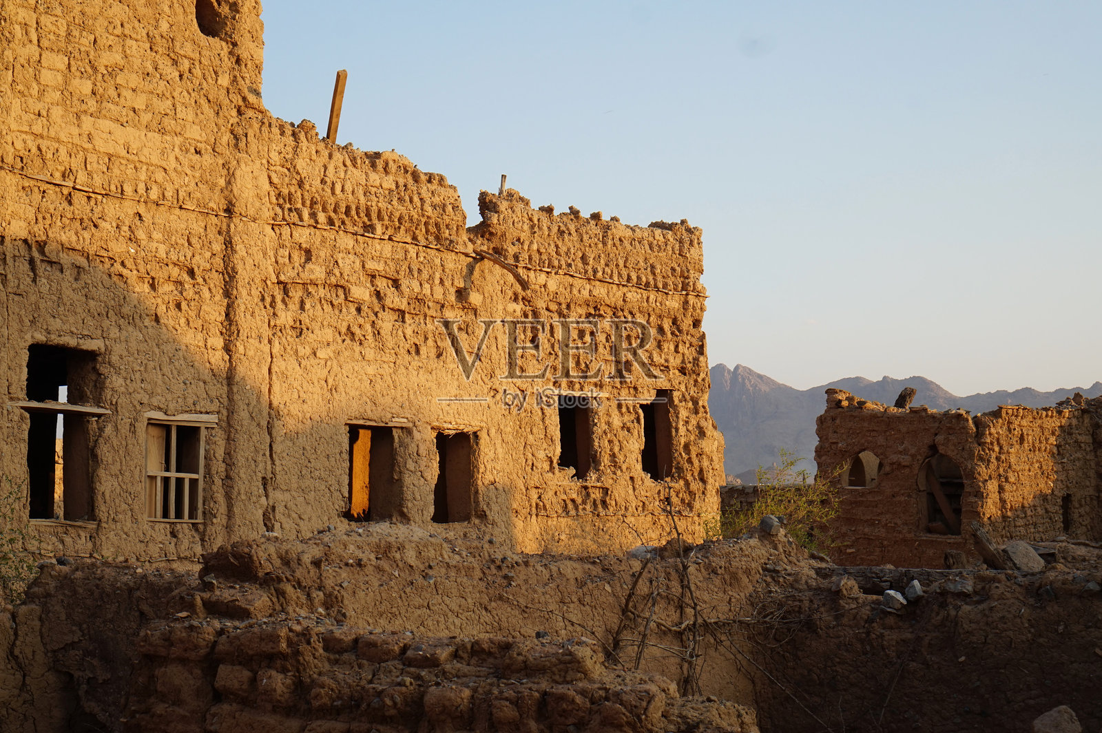 阿曼哈姆拉的古老废弃泥砖村遗址，背景是壮丽的岩山，夕阳下的美景照片摄影图片