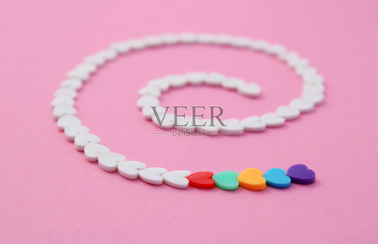 一排白色心形图案形成螺旋，最后以几颗不同颜色的心形结束。照片摄影图片