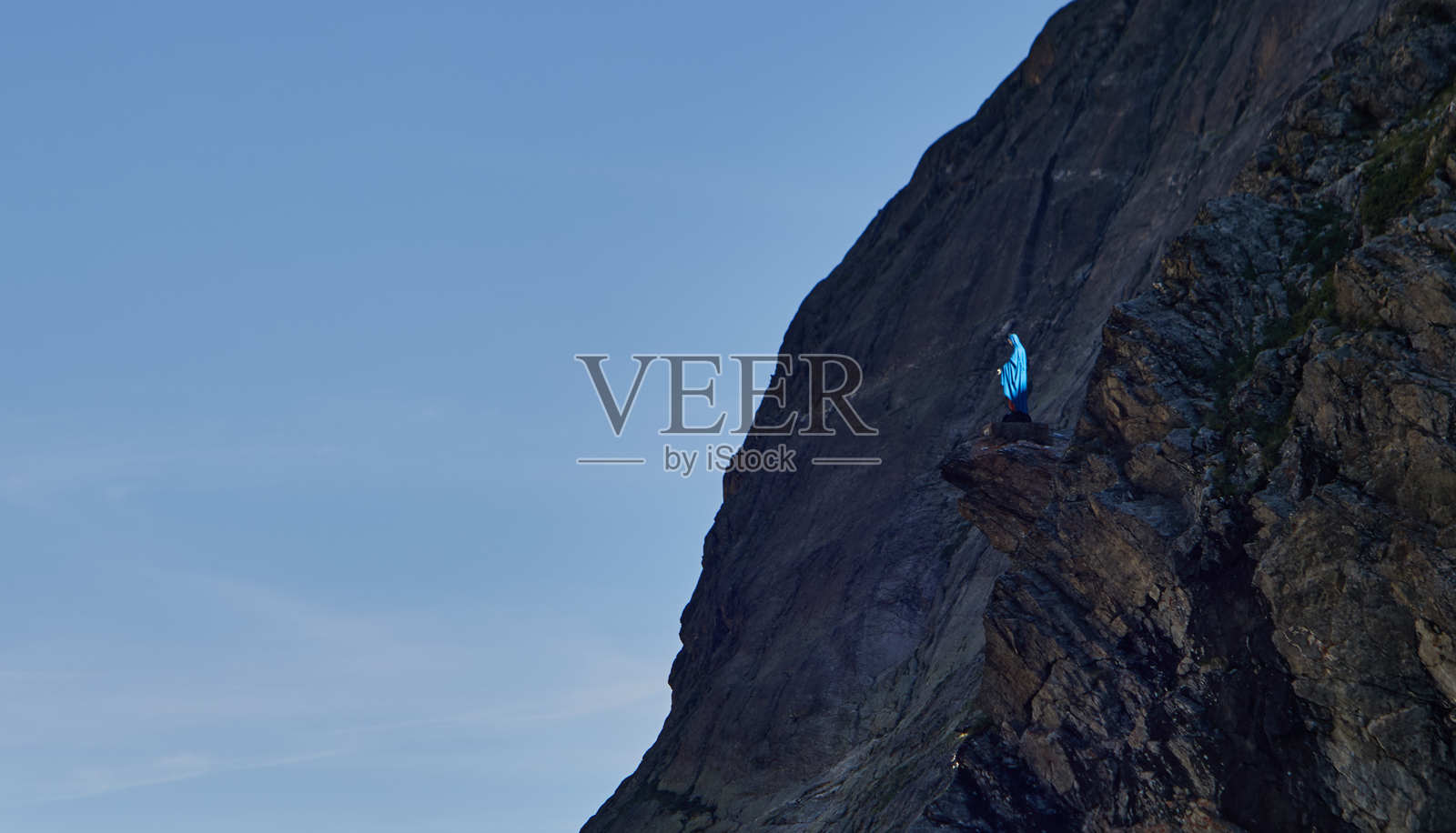 攀岩者在壮丽的山脉风景中攀爬岩壁，蓝天晴朗照片摄影图片