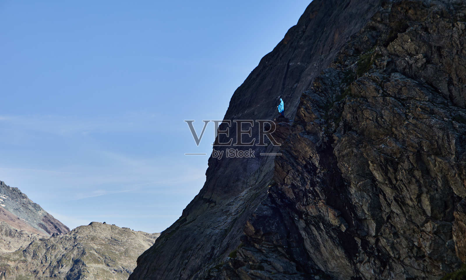 攀岩者在壮丽的山脉景观中攀爬岩壁，蓝天晴朗照片摄影图片