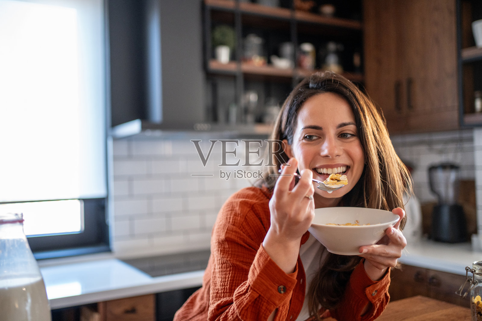 快乐的年轻女性在现代厨房里吃早餐麦片照片摄影图片