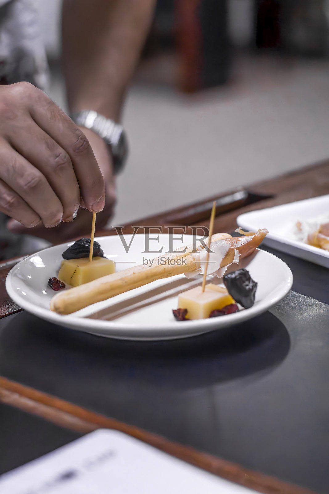 厨师正在准备美味的开胃菜，搭配意大利面包棒、奶酪和梅干。照片摄影图片