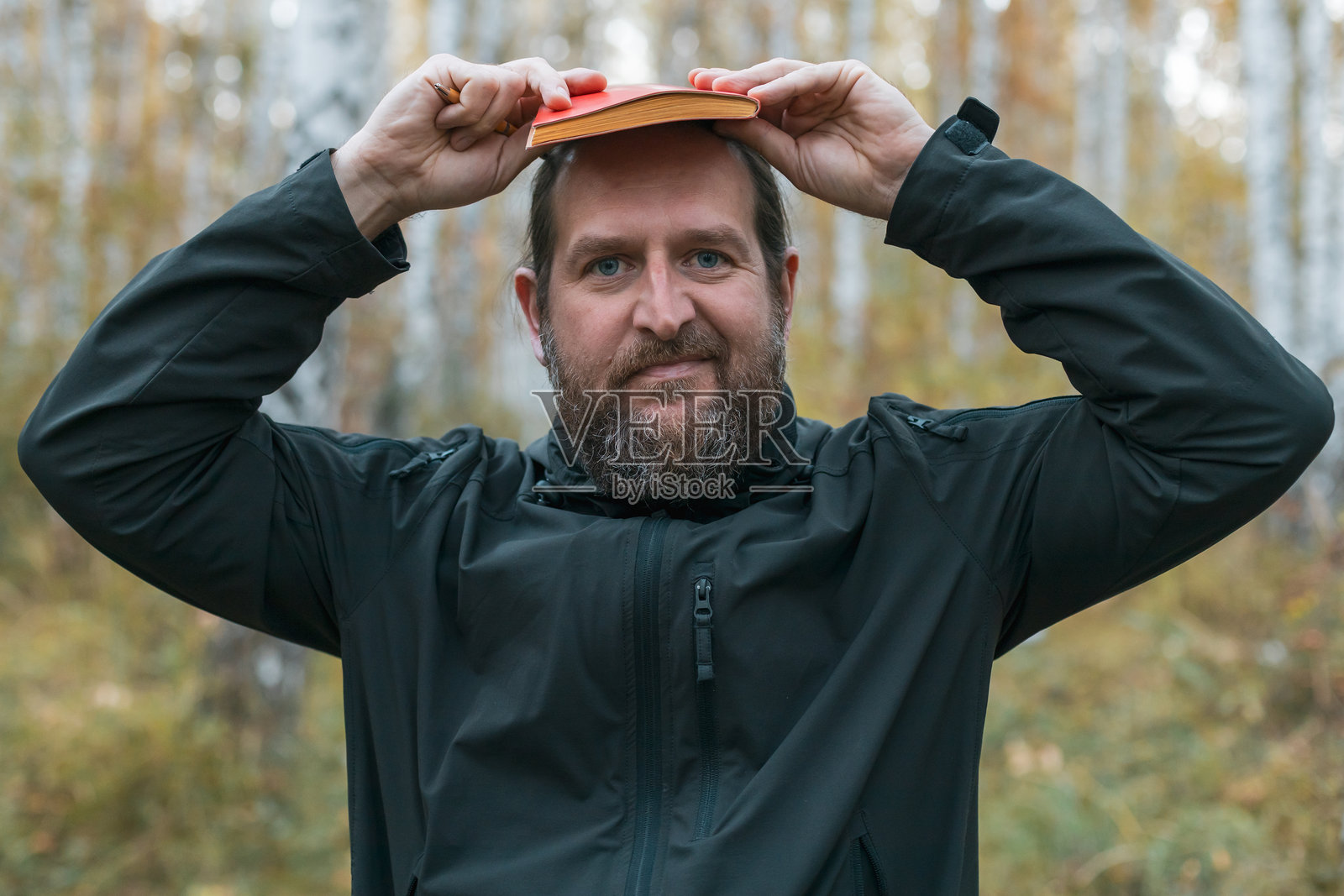 一个留着胡子的男人把一本书放在头上。照片摄影图片