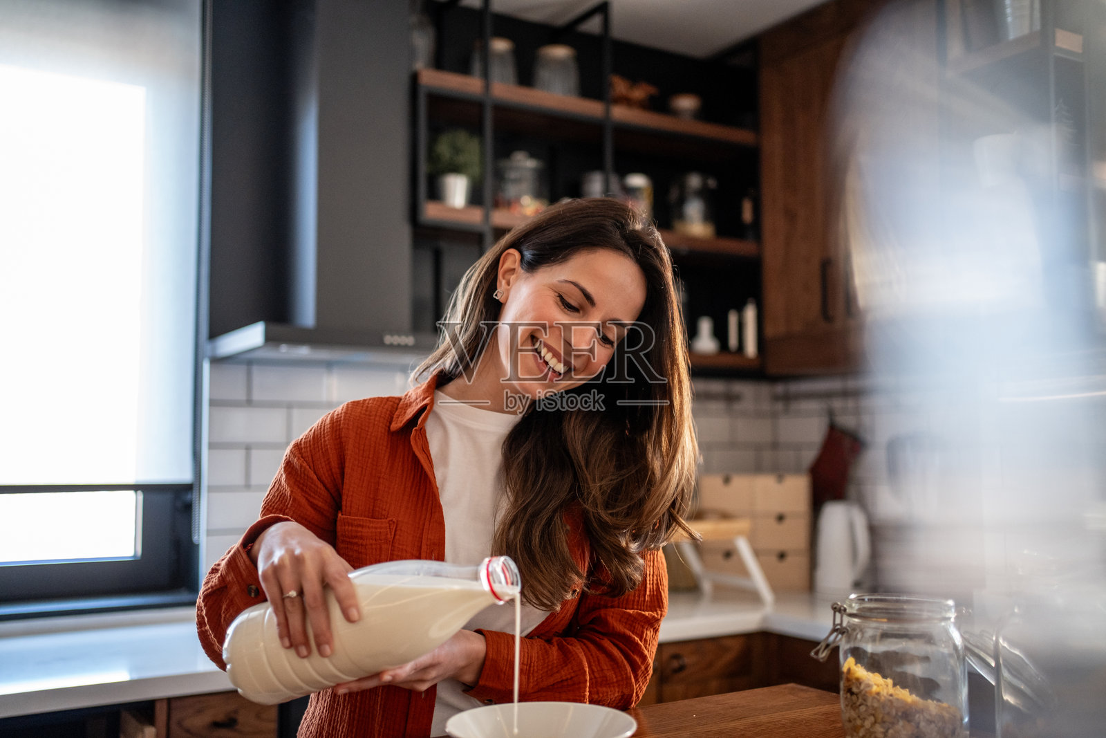 快乐的女人在厨房里把牛奶倒入碗中照片摄影图片