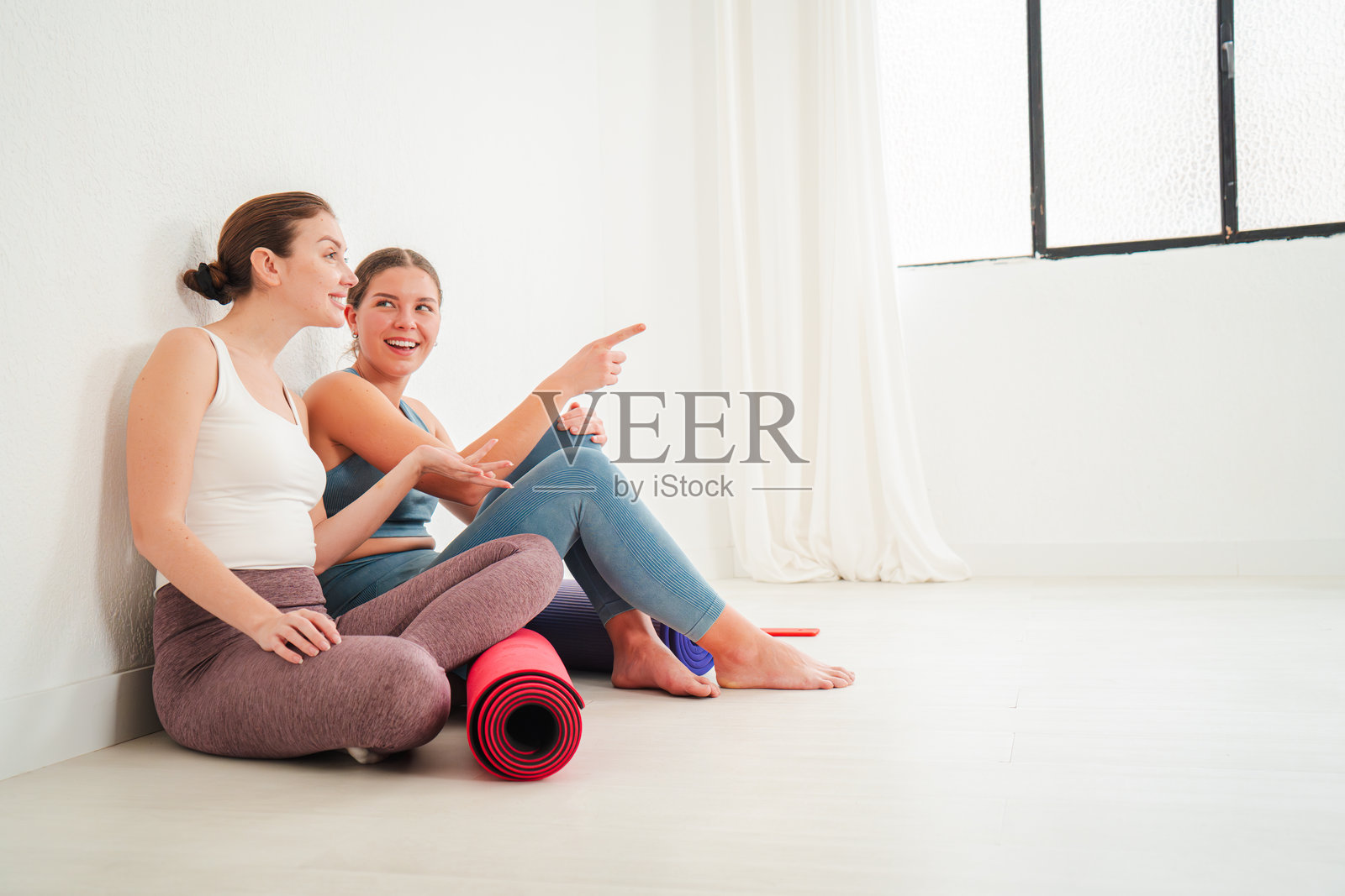 两位快乐的女性坐在地板上，进行着热烈的交谈，分享她们在一次充实的瑜伽课程后的想法和经历，创造了一个连接和友谊的时刻。照片摄影图片