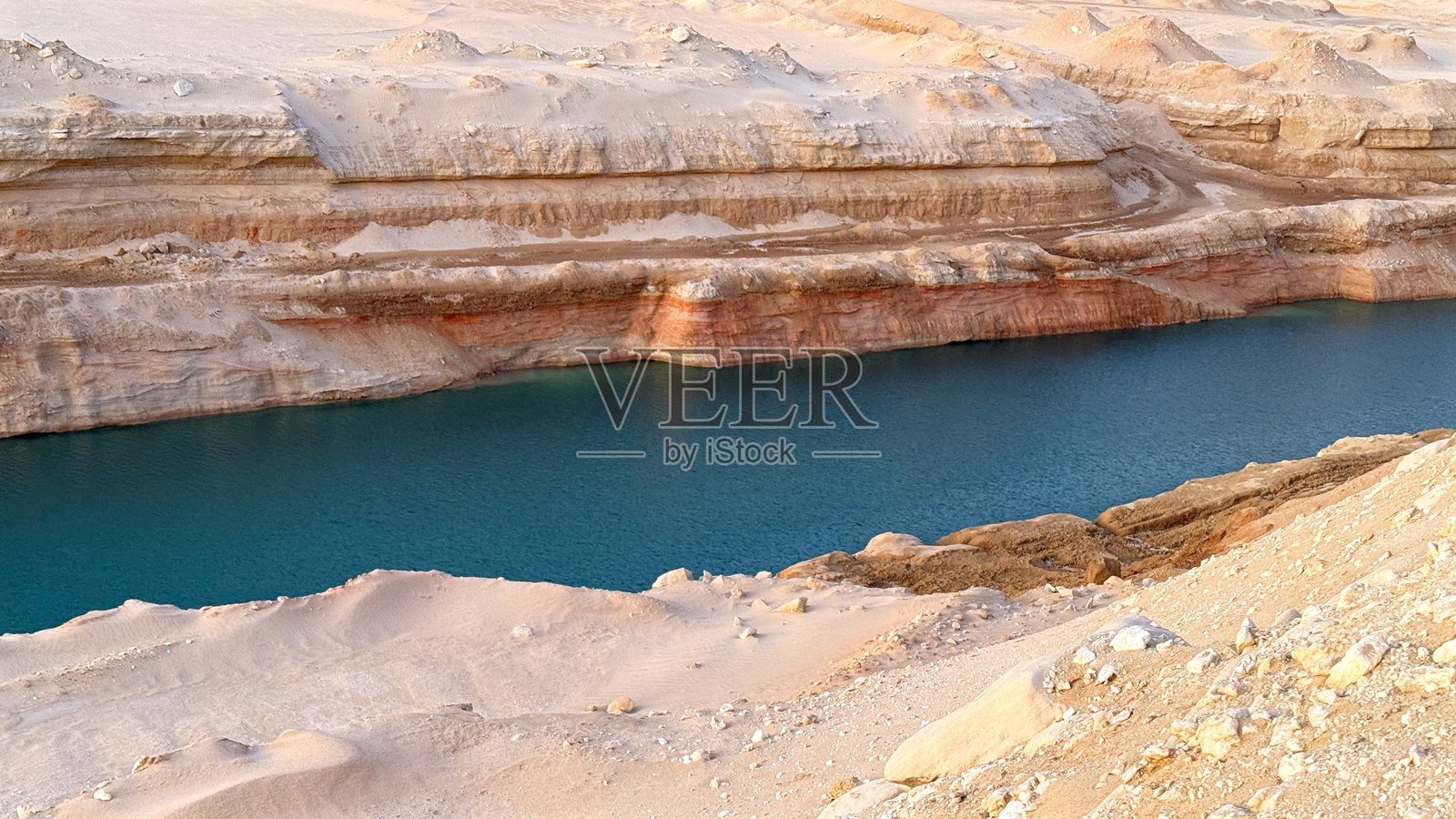 咸水湖在侵蚀的沙漠悬崖下形成，咸矿物塑造了湖边，沙漠地形在柔和的日落光辉下形成深深的侵蚀切口，位于干燥的沙漠区域。照片摄影图片