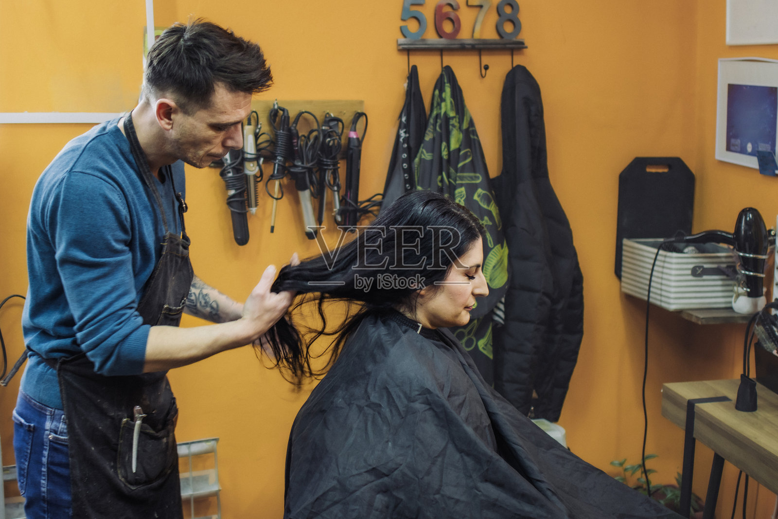 男发型师在美容院为女性顾客吹干头发。小型美发沙龙。照片摄影图片