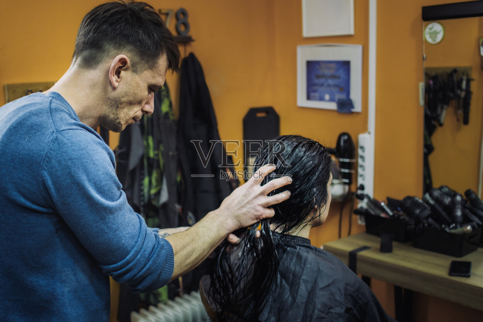男发型师在美容院为女性顾客吹干头发。小型美发沙龙。照片摄影图片
