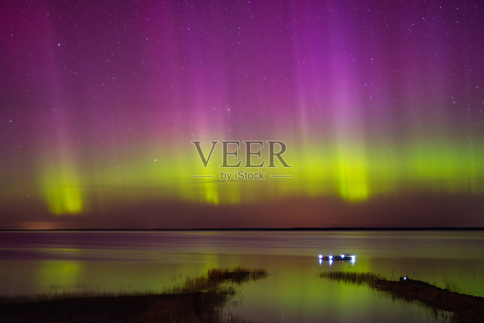 壮观的北极光在平静的湖面上闪烁，呈现出生动的绿色和紫色调，湖边的码头灯光闪烁，草地沿岸宁静。照片摄影图片