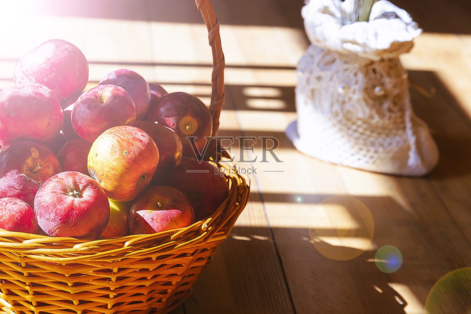 温暖阳光下，木地板上的藤编篮子里装着红苹果，乡村风格的舒适静物，充满丰收的氛围照片摄影图片